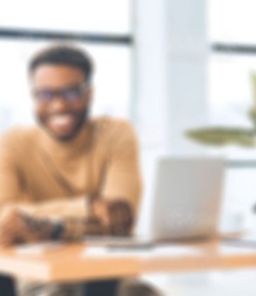 Blogger At Work. Smiling black man looking at camera, sitting at desk with laptop. Selective focus